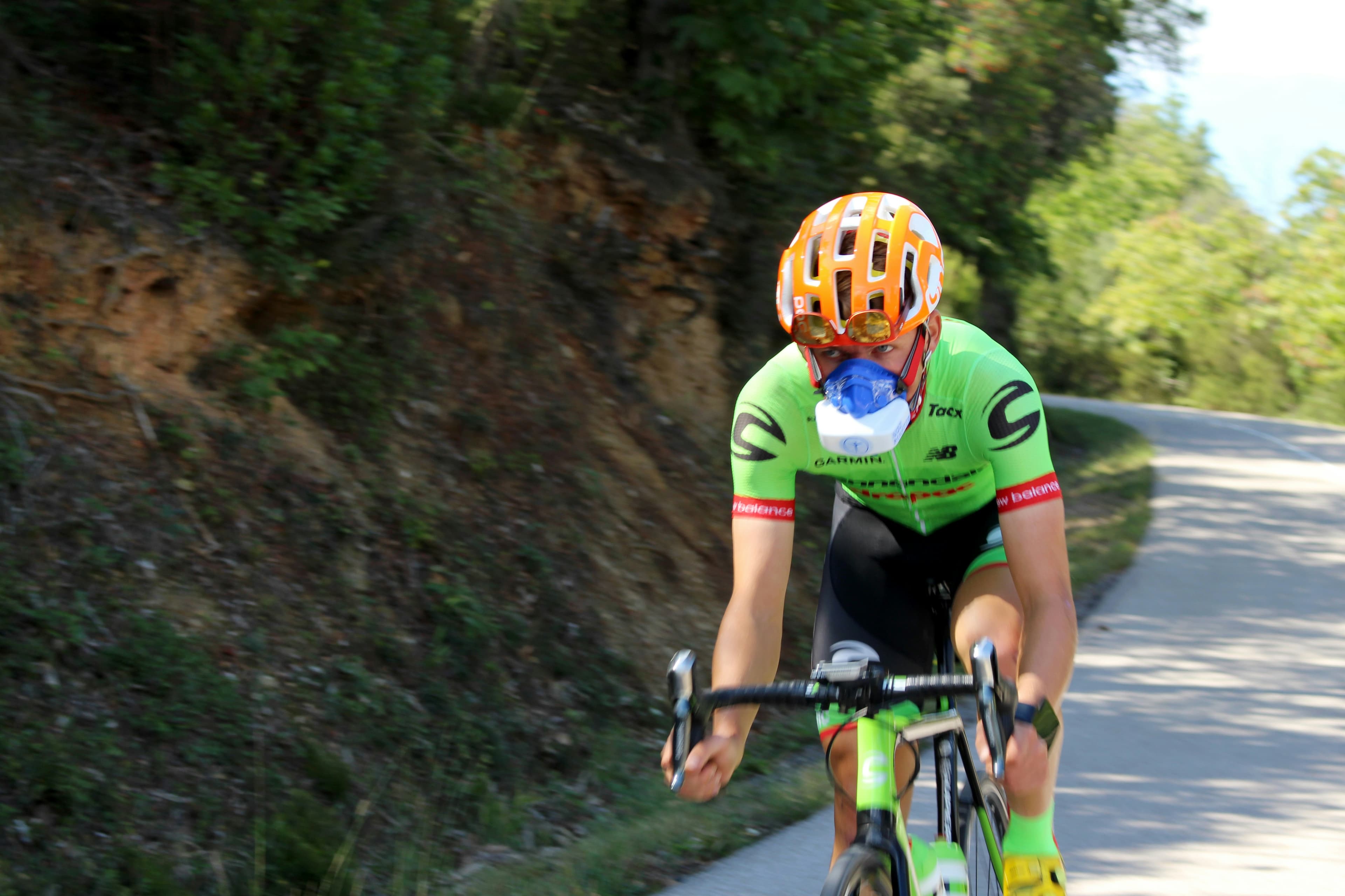 A cyclist wearing a metabolic testing mask, riding hard on a mountain road